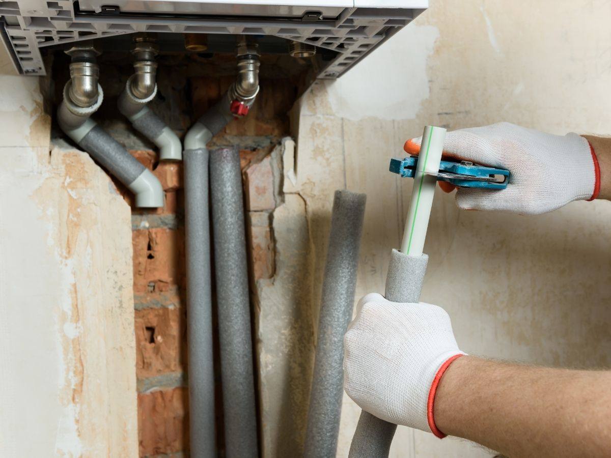 Technician cutting and fitting pipe below a wall mounted unit