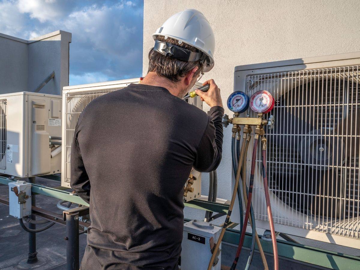 Technician checking refrigerant pressure gauges on a rooftop AC unit